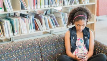 Serious mixed race girl on sofa in library texting on cell phone