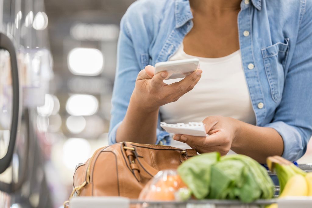 Unrecognizable supermarket customer uses smart phone and paper list