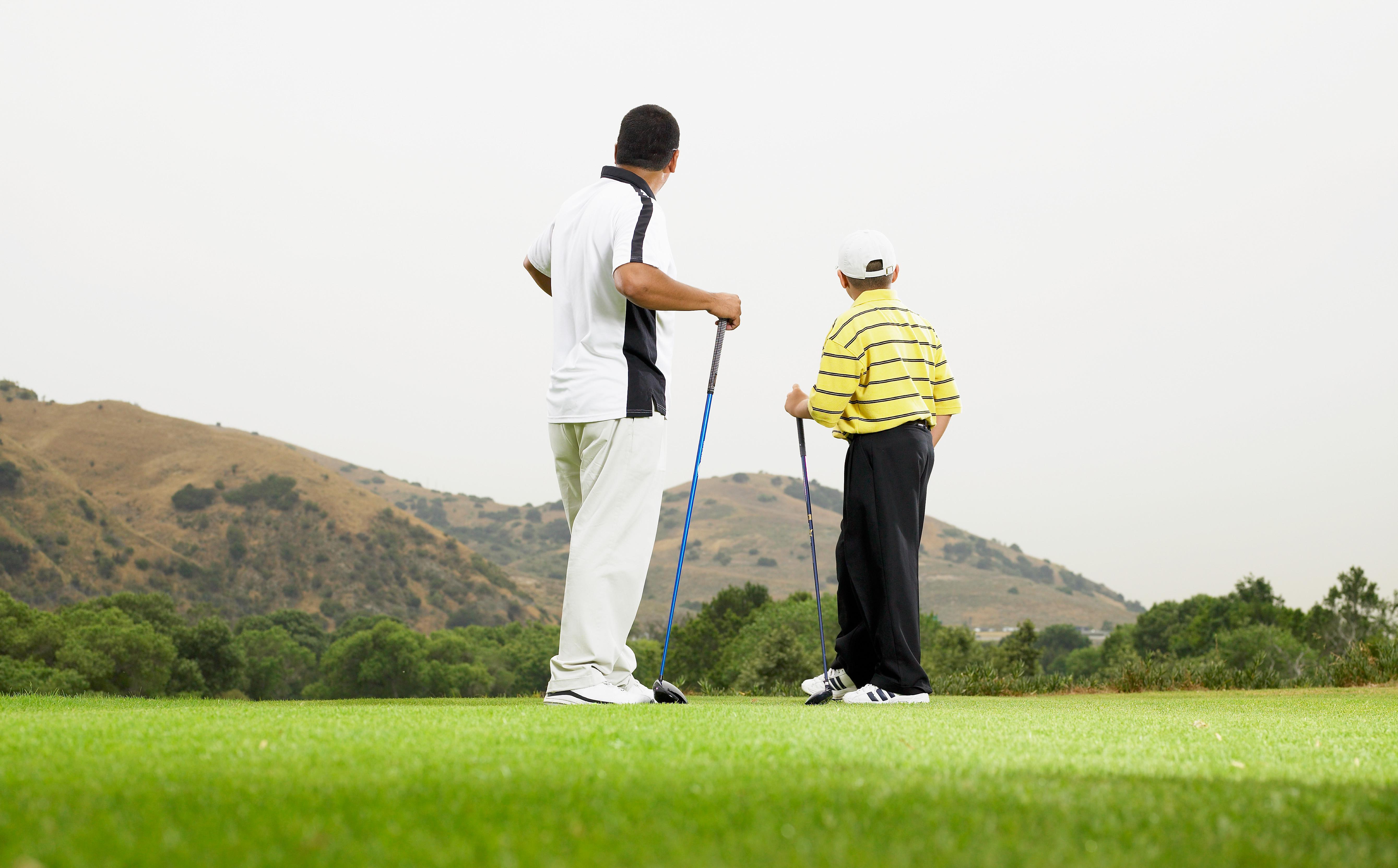 Father and son (8-10) playing golf together, rear view
