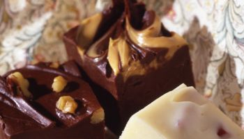 A close-up view of three pieces of fudge with nuts and peanut butter and white chocolate sitting on a patterned napkin