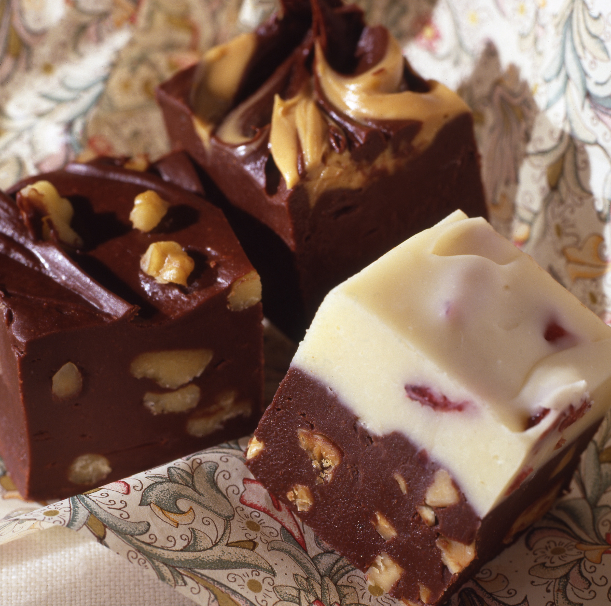 A close-up view of three pieces of fudge with nuts and peanut butter and white chocolate sitting on a patterned napkin