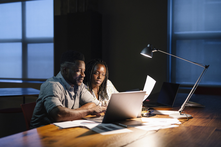 Business people working late at laptop in dark office