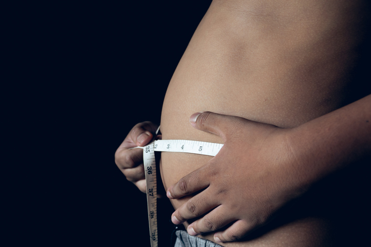 Midsection Of Shirtless Fat Boy Measuring Stomach With Tape Measure Over Black Background