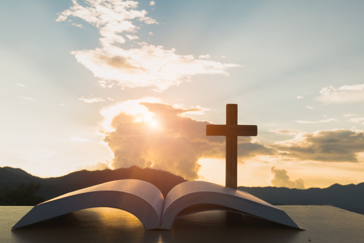 Close-Up Of Bible With Cross Against Sky During Sunset