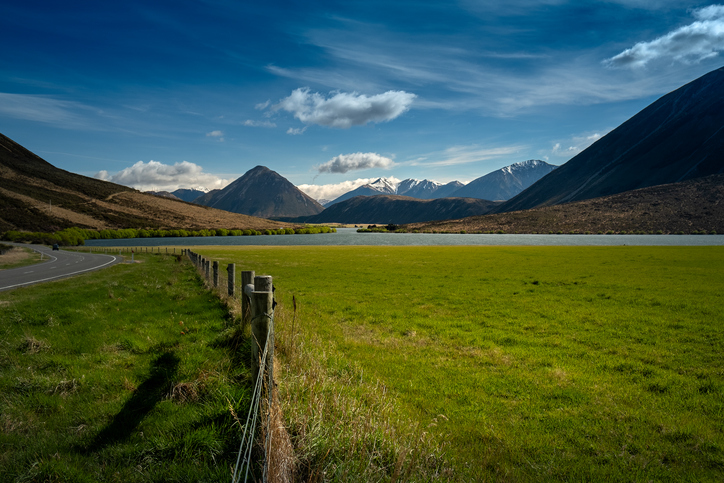 Landscape of mountains, road, grass field with Lake Pearson on a sunny day with blue sky in New Zealand