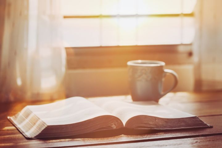 an open bible with a cup of coffee for morning devotion on wooden table