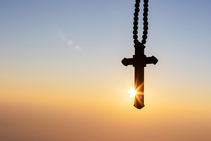 Silhouettes of crucifix necklace symbol with bright sunbeam on the colorful sky background