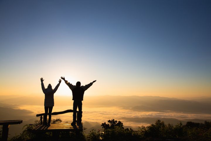 Silhouettes of a Christian man and woman spreading their arms to ask for blessings on a mountain. Together for recovery, providing emotional support. Praying for love and faith in religion.
