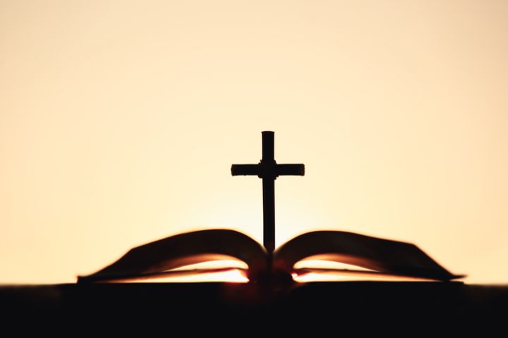 Jesus' holy cross, Bible and brightly shining sunset silhouette worship, prayer and meditation church background